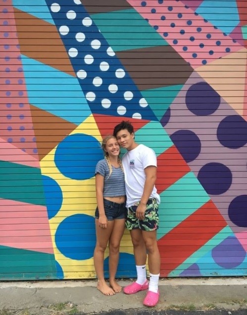 Isaiah Woo and Kayla Nordeman stand outside a building with colorful art in downtown Richmond. Isaiah is wearing his crocs with socks and trying to start a new style. 