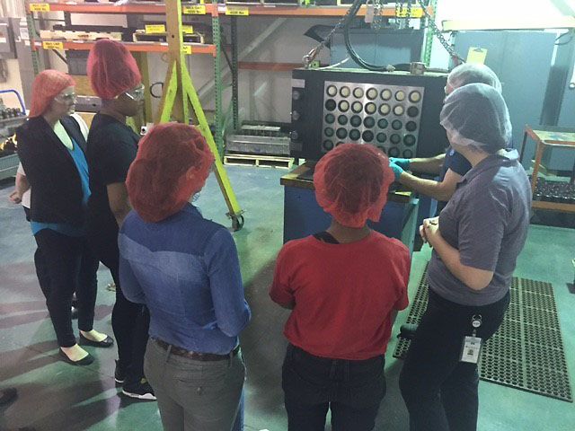 Students observe factory workers explaining their jobs with interest at Manufacturing Day.