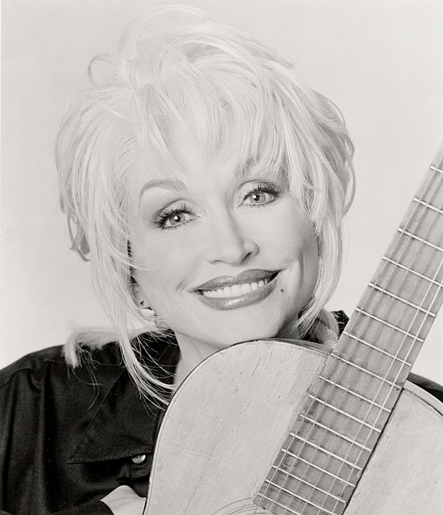 Dolly Parton poses with her guitar. Dennis Carney, Public domain, via Wikimedia Commons