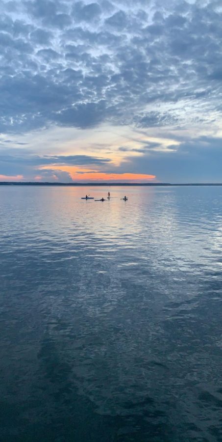 Blue clouds reflect off the sun kissed York River as my family shadows drift toward the setting sun. Seen in the picture is my aunt on the left kayak, my brother who is holding onto a paddle board, my sister standing and paddling on her paddle board, and my cousin kayaking on the right.