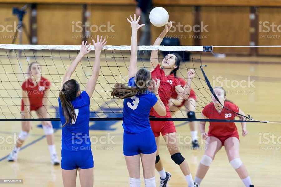 Asian high school volleyball player spikes volleyball against female opponents