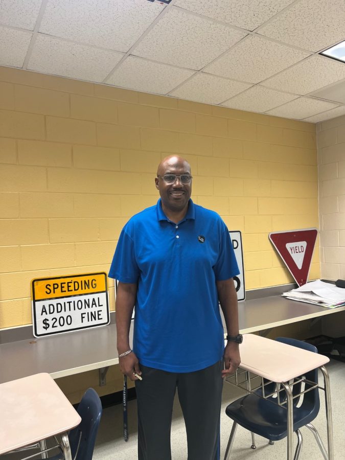 Mr. Hundley smiling in front of his Driver's Ed class road signs.