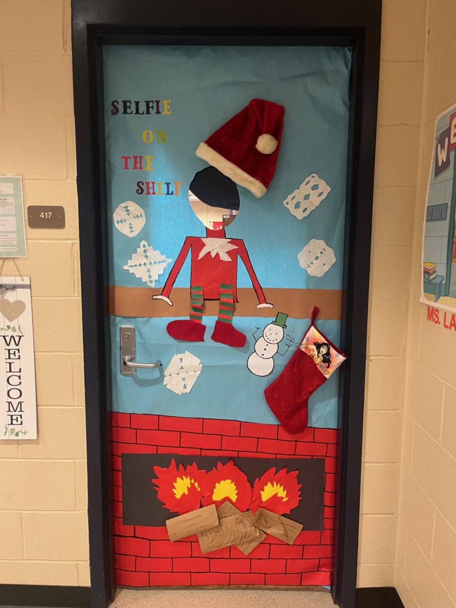 Mrs. Lanham's door has a genius Elf-inspired play on words, with the door having the text 'Selfie on the Shelf' referencing the ever popular elf on the shelf toys!